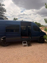 This RV rental, a dark blue camper van, has its side doors open with a step stool, inviting road trip adventures.