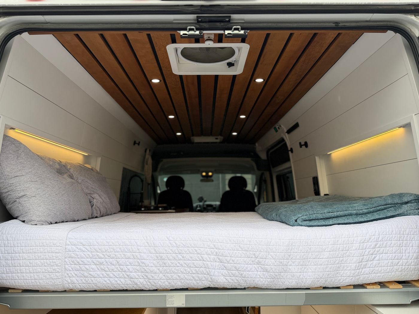 Cozy camper van interior for your next RV rental, featuring a comfortable bed, warm lighting, and a stylish wooden ceiling. — photo 9