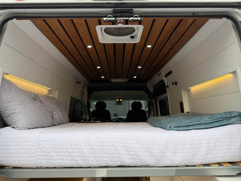 Cozy camper van interior for your next RV rental, featuring a comfortable bed, warm lighting, and a stylish wooden ceiling. — photo 9