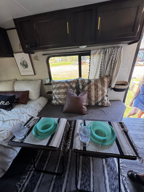 Inviting RV rental interior with a cozy bed, dining area set for two, and bohemian decor. Perfect for travel adventures.