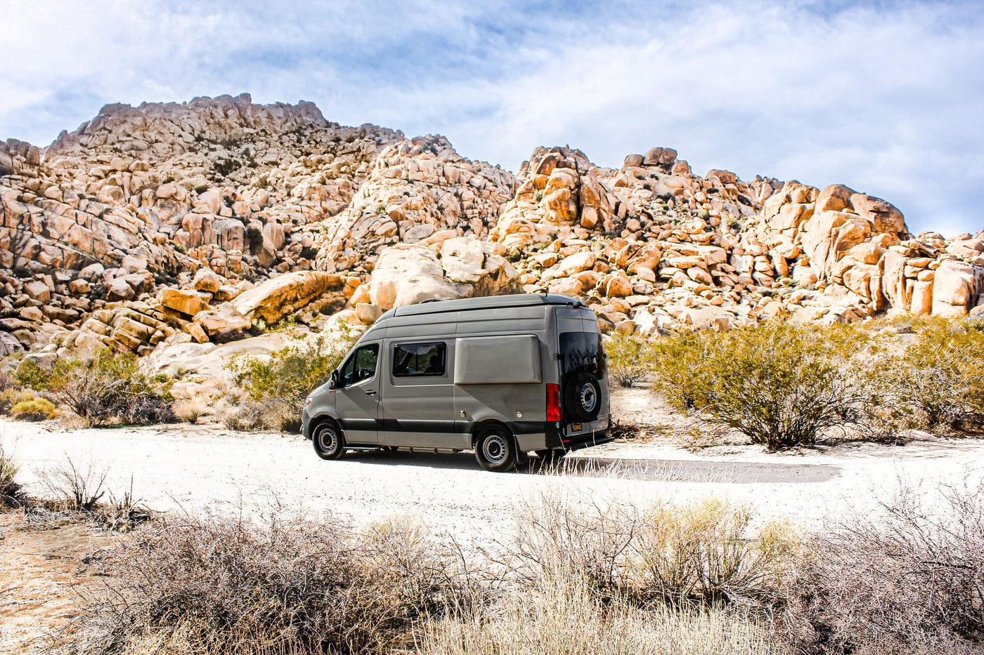A grey RV rental is parked on a dirt road amidst large desert rock formations under a cloudy sky. — photo 10