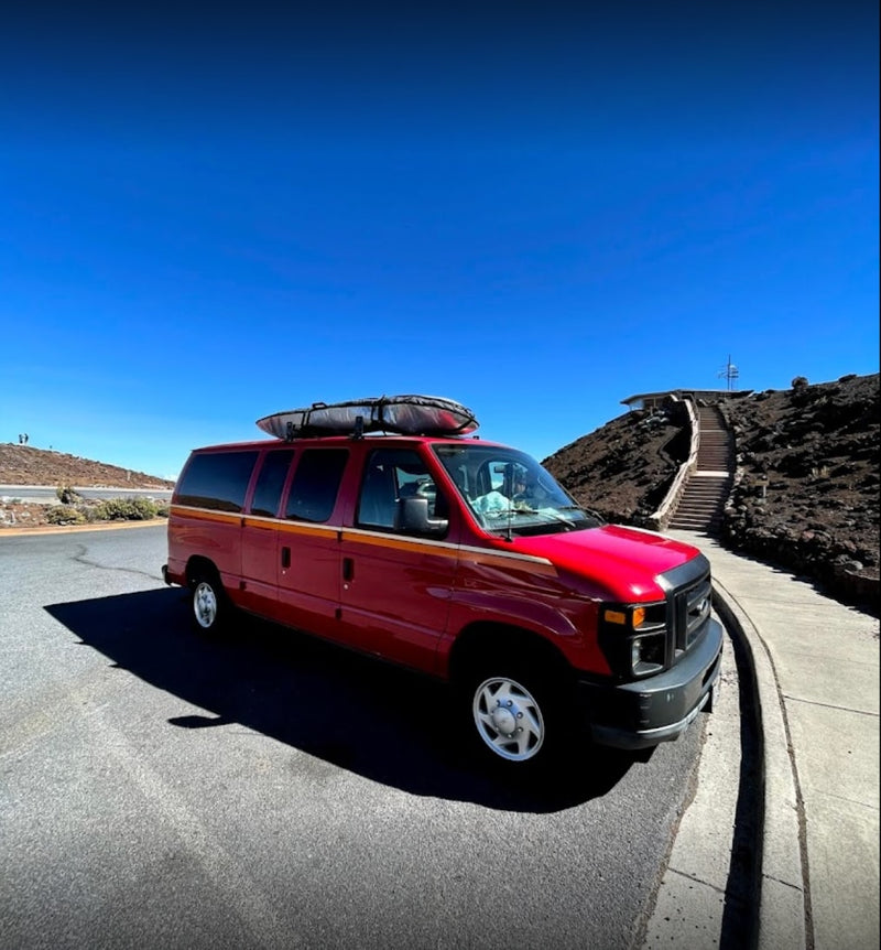 Red **RV rental** van with surfboard on roof, parked on a mountain road with steps leading to a scenic viewpoint under a clear blue sky. — photo 17