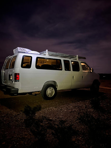 Night shot of a white camper van with a rooftop AC & roof rack. Ideal for an RV rental adventure under cloudy skies.