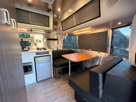 Modern RV rental interior: aluminum walls, black seating, compact kitchen & dinette.