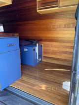Inside an RV rental: rich wood walls & floor, sleek blue cabinets. A cozy, functional camper interior.