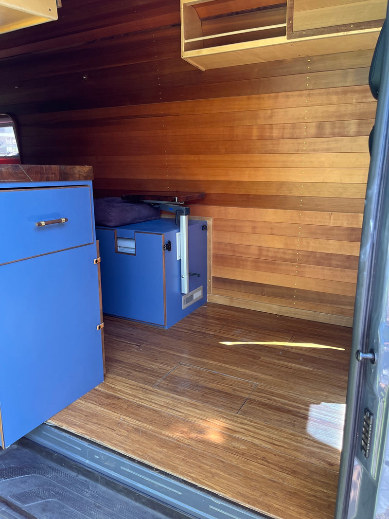 Inside an RV rental: rich wood walls & floor, sleek blue cabinets. A cozy, functional camper interior. — photo 14