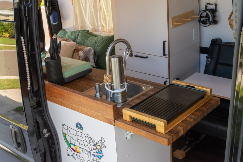 View inside a modern RV rental, featuring a well-equipped compact kitchen with sink, griddle, and comfy living space. — photo 9
