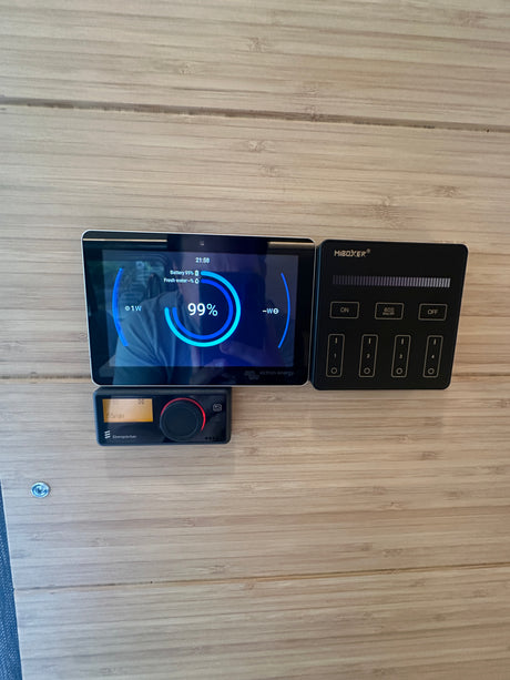 RV rental dashboard showing Victron energy display (battery 99%), Eberspächer heater, and MiBoxer lighting controls on a wood panel.