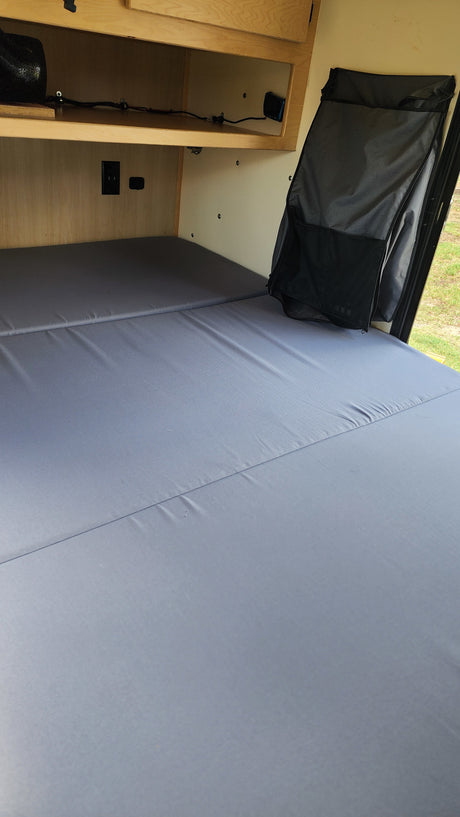 RV rental interior showing a grey sleeping area, overhead shelf with power outlets, and a hanging storage organizer.