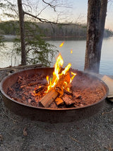 Lakeside campfire blazing in a metal pit, perfect for a relaxing evening during your RV rental trip. Enjoy nature's warmth!