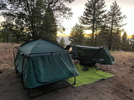 Two elevated tent cots at a sunset campsite. A unique camping experience, perfect as an alternative or addition to an RV rental.