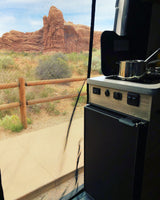 RV rental interior showing a compact camper kitchen, with a stunning desert view of red rock formations through a mesh screen.