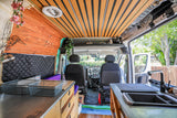 RV rental: Bright camper van interior with wooden slat ceiling, kitchen, storage, and driver's cabin.
