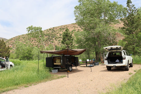 Scenic rv rental camping: Teardrop trailer, awning, SUV, and picnic table in a lush, hilly natural camp.