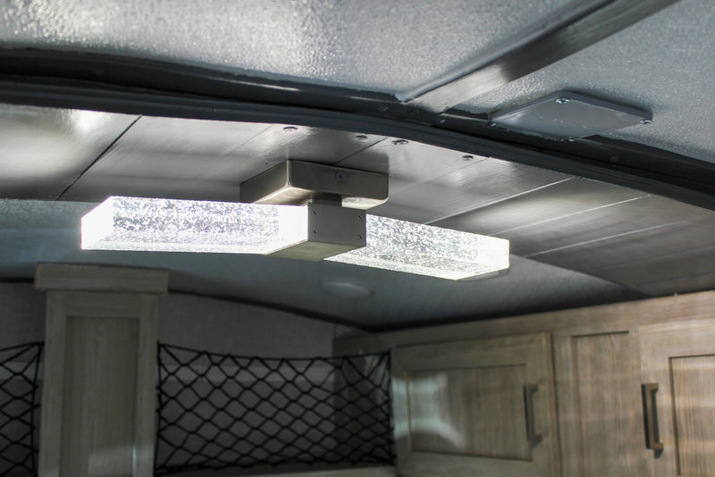 Illuminated glass fixture in an RV rental interior, highlighting ceiling panels, storage nets, and cabinetry. — photo 16
