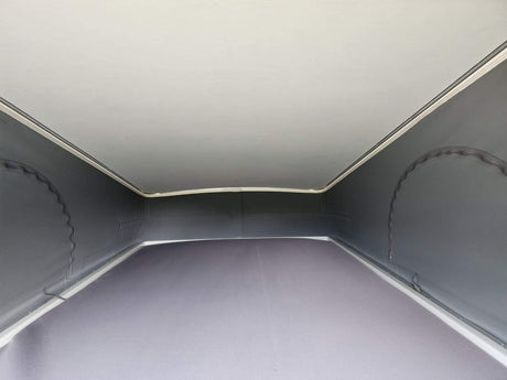View inside a light grey pop-top RV rental, showcasing the canvas sidewalls, solid ceiling, and bed area.