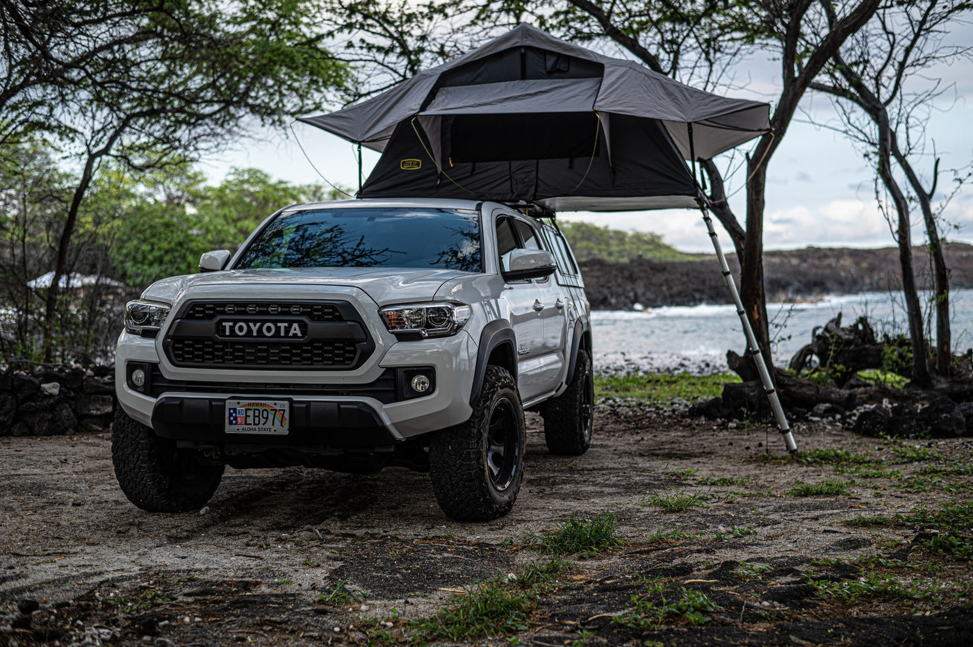 White Toyota Tacoma with a gray rooftop tent set up for coastal camping on Hawaii's lava rocks. Your adventure RV rental. — photo 5