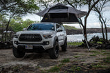 White Toyota Tacoma with a gray rooftop tent set up for coastal camping on Hawaii's lava rocks. Your adventure RV rental.