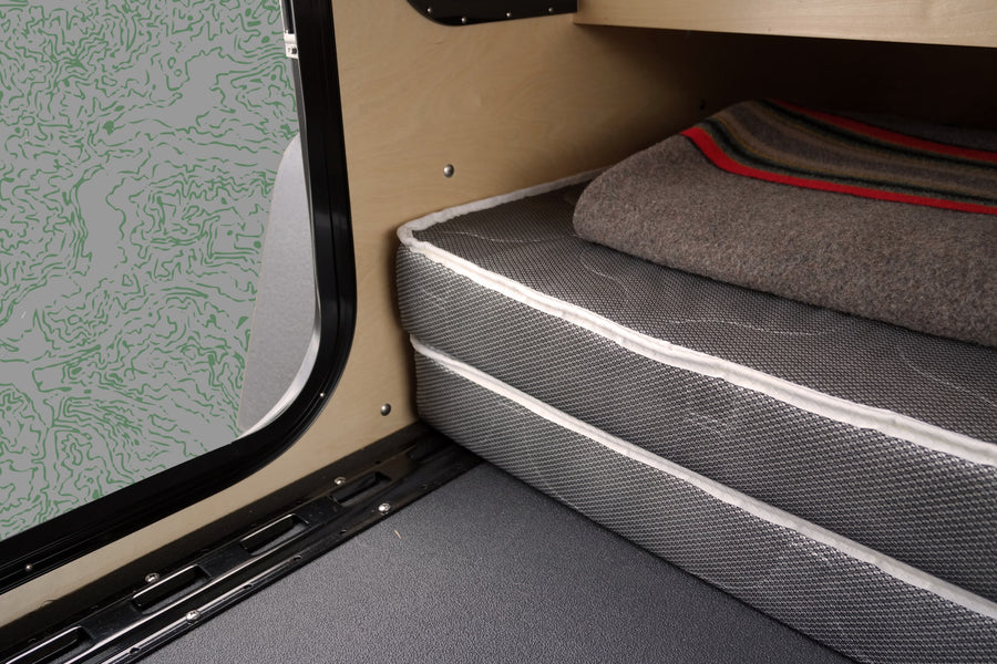 RV rental interior: Comfortable mattress, warm blanket, wooden panels, and a decorative map-patterned wall by the entry.