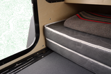 RV rental sleeping area showing a comfortable mattress, cozy blanket, and a unique window design, ideal for camping.