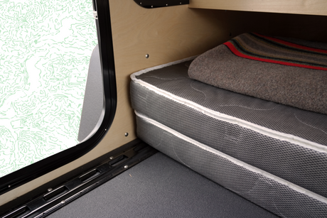 RV rental sleeping area showing a comfortable mattress, cozy blanket, and a unique window design, ideal for camping.