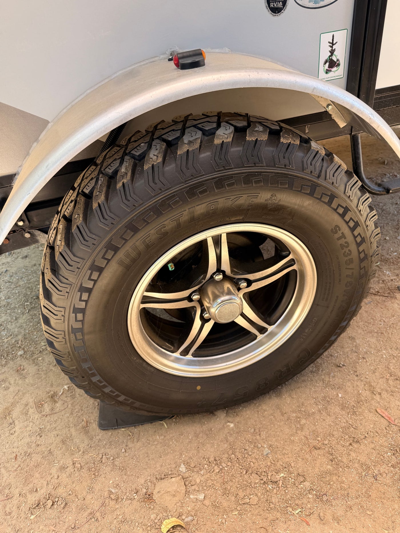 A robust Westlake ST235/75R15 tire and silver wheel on an RV rental, clearly showing the rugged tread and dirt environment. — photo 7