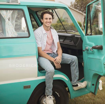 A smiling young man sits in the open doorway of a teal vintage camper van. Perfect RV rental for your next adventure!
