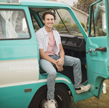 A smiling young man sits in the open doorway of a teal vintage camper van. Perfect RV rental for your next adventure!
