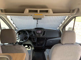 RV rental's front cabin interior features a dashboard, front seats, and a pleated sunshade covering the windshield.