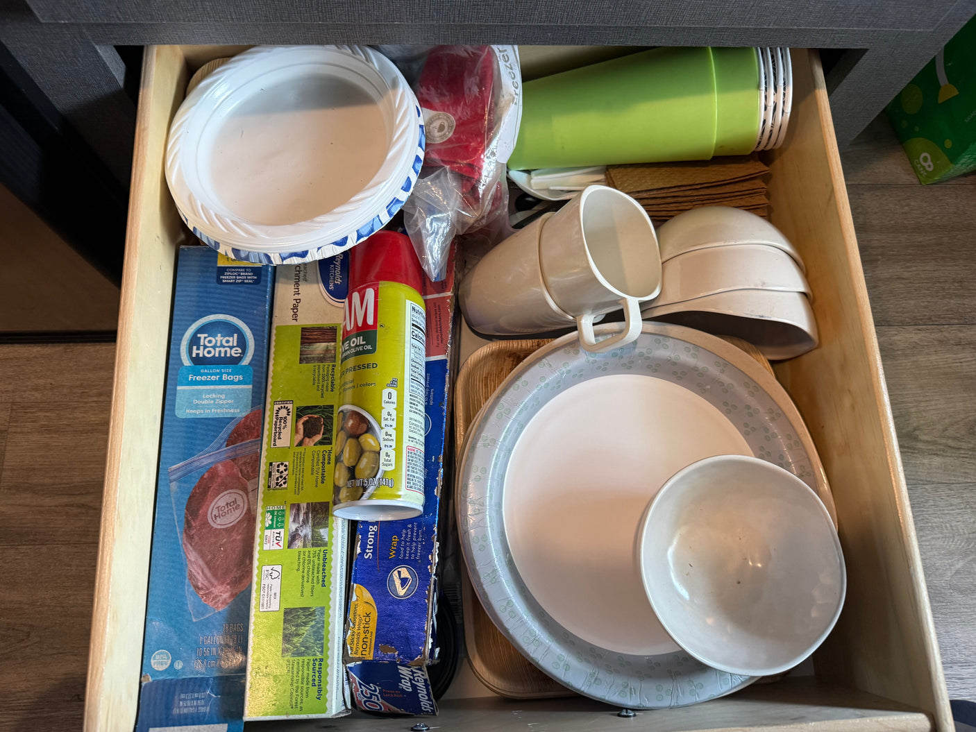RV rental kitchen drawer with camping supplies: paper plates, plastic cups, freezer bags, cooking spray, and reusable bowls.