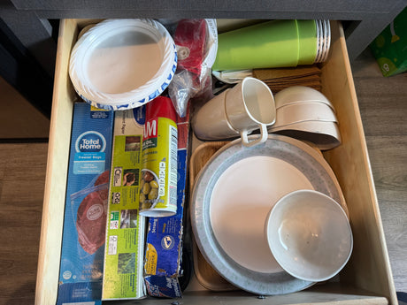 RV rental kitchen drawer with camping supplies: paper plates, plastic cups, freezer bags, cooking spray, and reusable bowls.