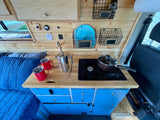 This cozy RV rental's kitchen, featuring a sink, stove, blue cabinets, and a comfy bed. Perfect for mobile living.