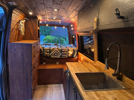 Step inside this charming RV rental: a rustic wooden camper van conversion featuring a bed, kitchen, and ambient lighting.