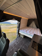Inside an RV rental: a modern camper van conversion with a cozy bed, kitchen, and scenic mountain views.