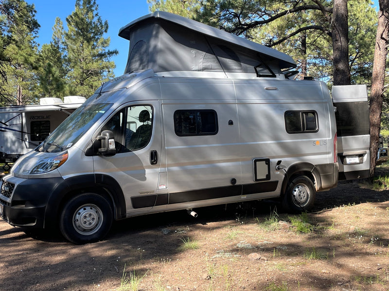 This light grey pop-top camper van, possibly an rv rental, is set up at a wooded campsite, plugged in for adventure. — photo 3