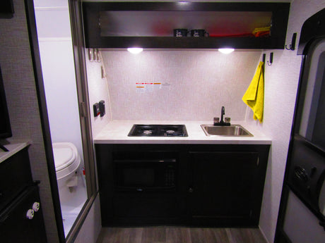 Compact RV rental kitchen featuring a sink, stove, microwave, and storage. Ideal for travel, with a visible bathroom.
