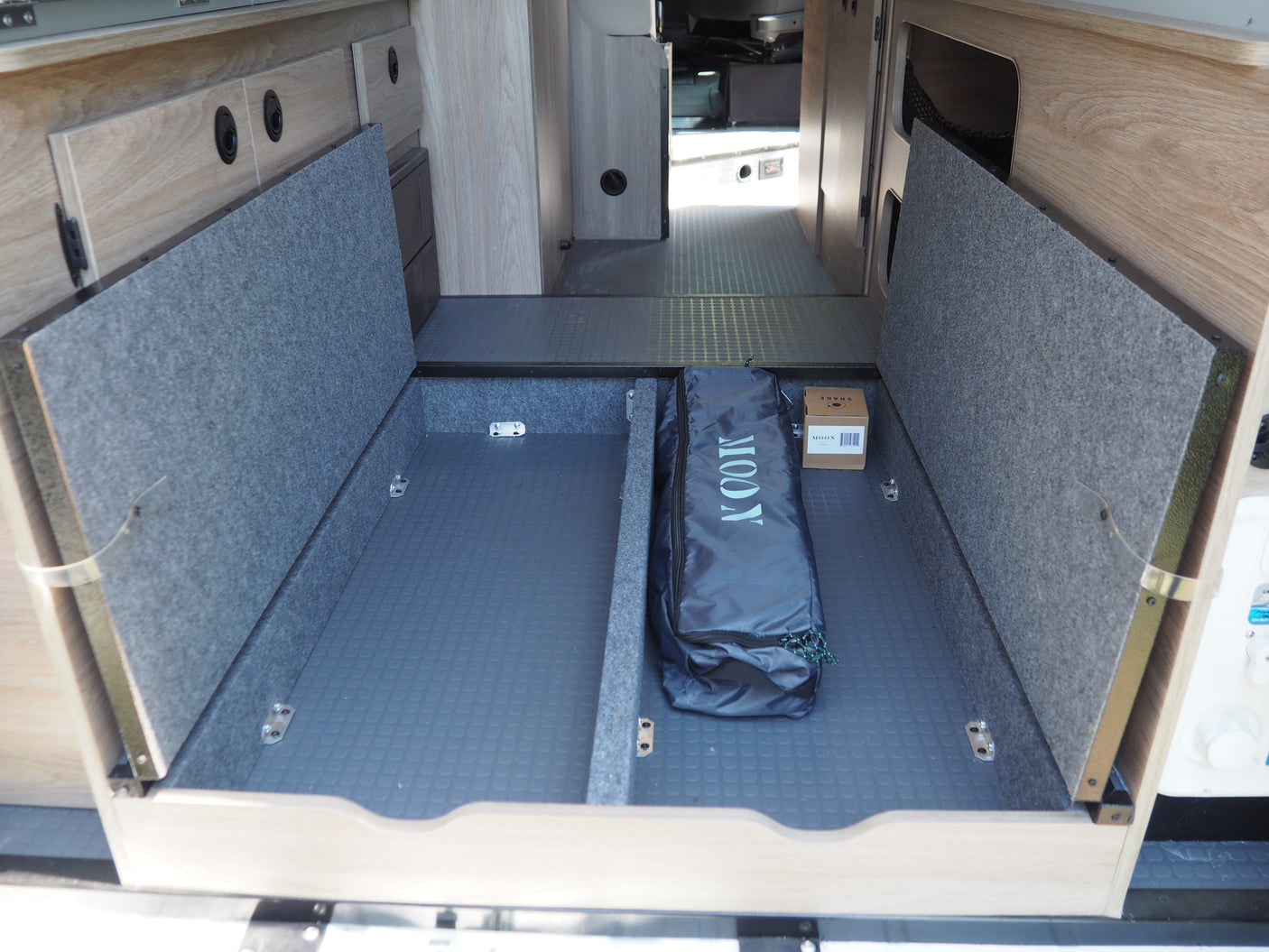 RV rental's rear storage, showing open compartments with a textured floor, a 'MOON' bag, and a box.