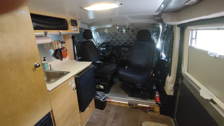 RV rental: Inside a camper van, showing a compact kitchen with sink, front seats, and insulated window covers.