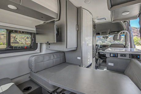 Inside a sleek rv rental: dinette, kitchen sink, TV, and scenic window view, ready for your next adventure.