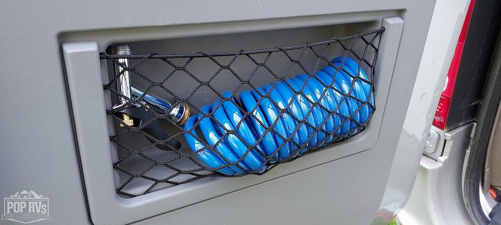 RV rental: Compact outdoor shower featuring a chrome head and coiled blue hose in a convenient storage net.
