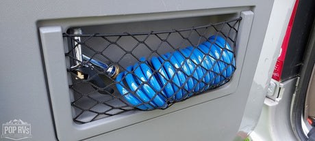 RV rental: Compact outdoor shower featuring a chrome head and coiled blue hose in a convenient storage net.