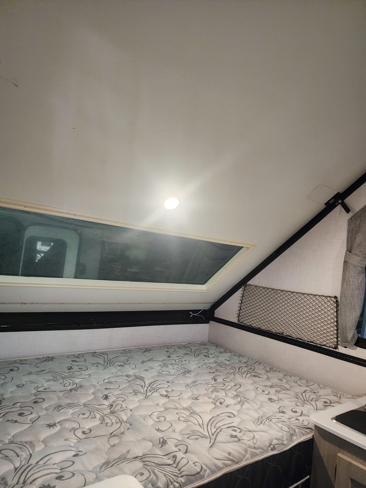 RV rental interior: A cozy sleeping area with a patterned mattress, overhead window/skylight, and storage net. — photo 5