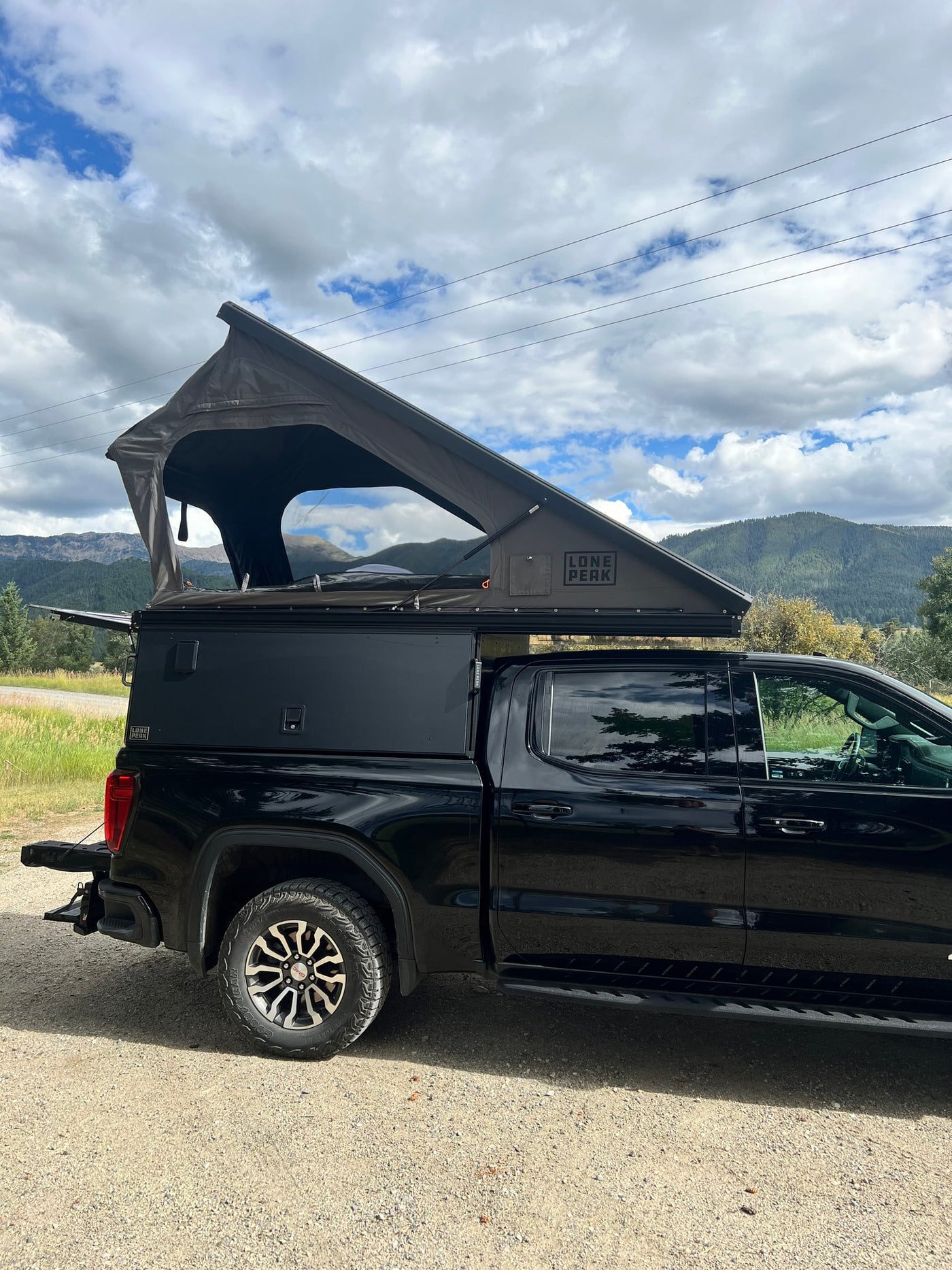 Black GMC truck RV rental featuring a Lone Peak pop-up camper, ready for mountain overlanding. — photo 14