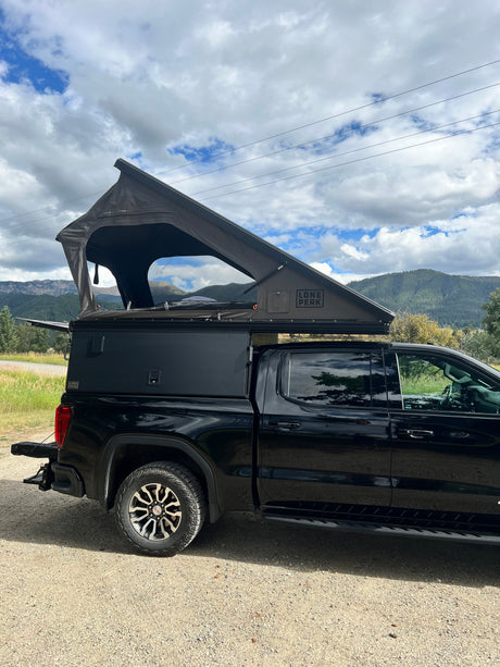 Black GMC truck RV rental featuring a Lone Peak pop-up camper, ready for mountain overlanding.