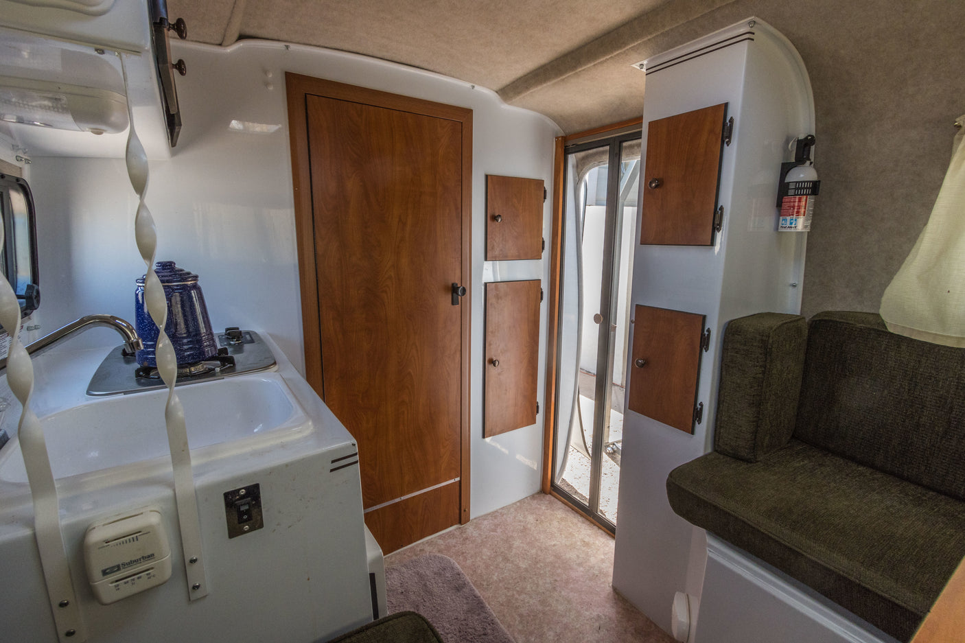 RV rental interior: kitchen with sink & stove, wood cabinets, green sofa, and an exit door. Compact, functional space.