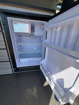 New RV rental fridge, spotless and ready for groceries, features freezer and adjustable shelves.
