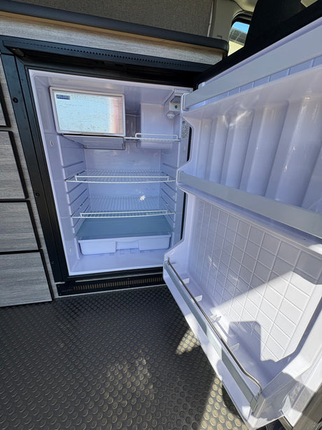 New RV rental fridge, spotless and ready for groceries, features freezer and adjustable shelves.