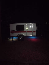 This white "Navigator" camper at night, illuminated by blue and red ground lights, is ready for your next RV rental adventure.
