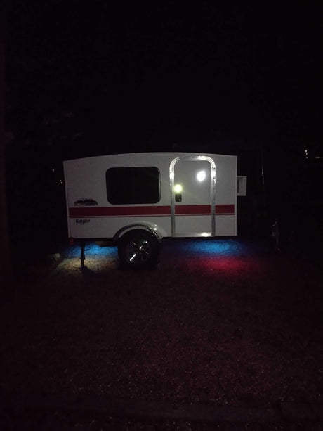 This white "Navigator" camper at night, illuminated by blue and red ground lights, is ready for your next RV rental adventure.