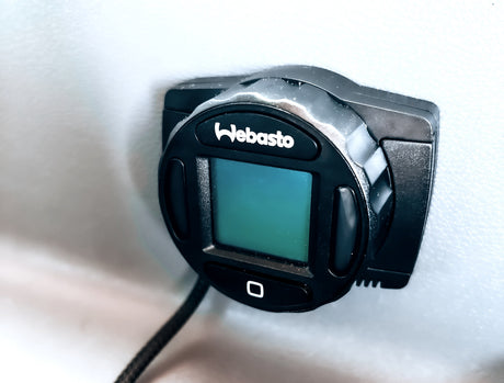 Webasto climate control panel in an RV rental. This black unit with a display screen is mounted on a light wall.